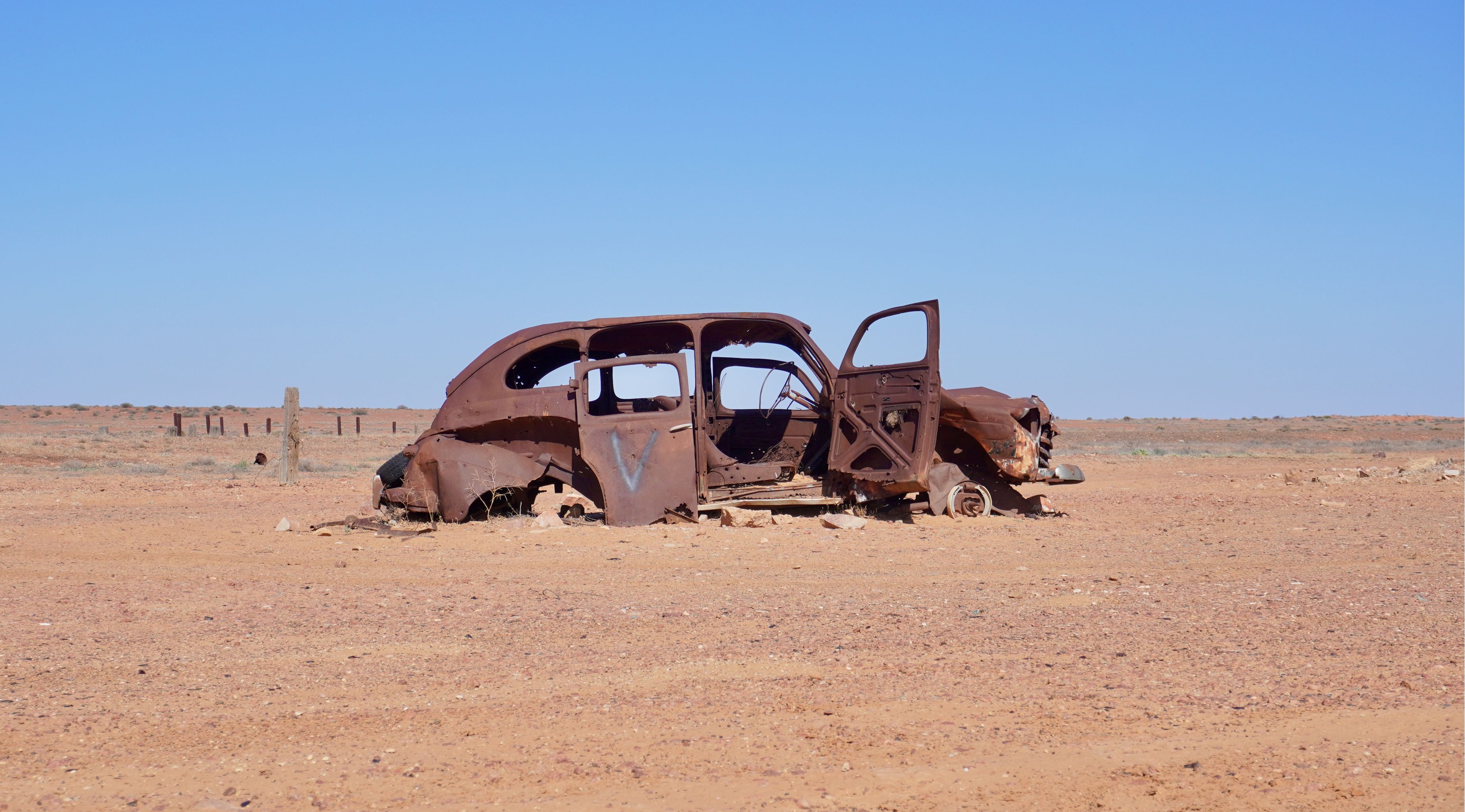 The rusty carcass of an abandonned car on the side of the road.