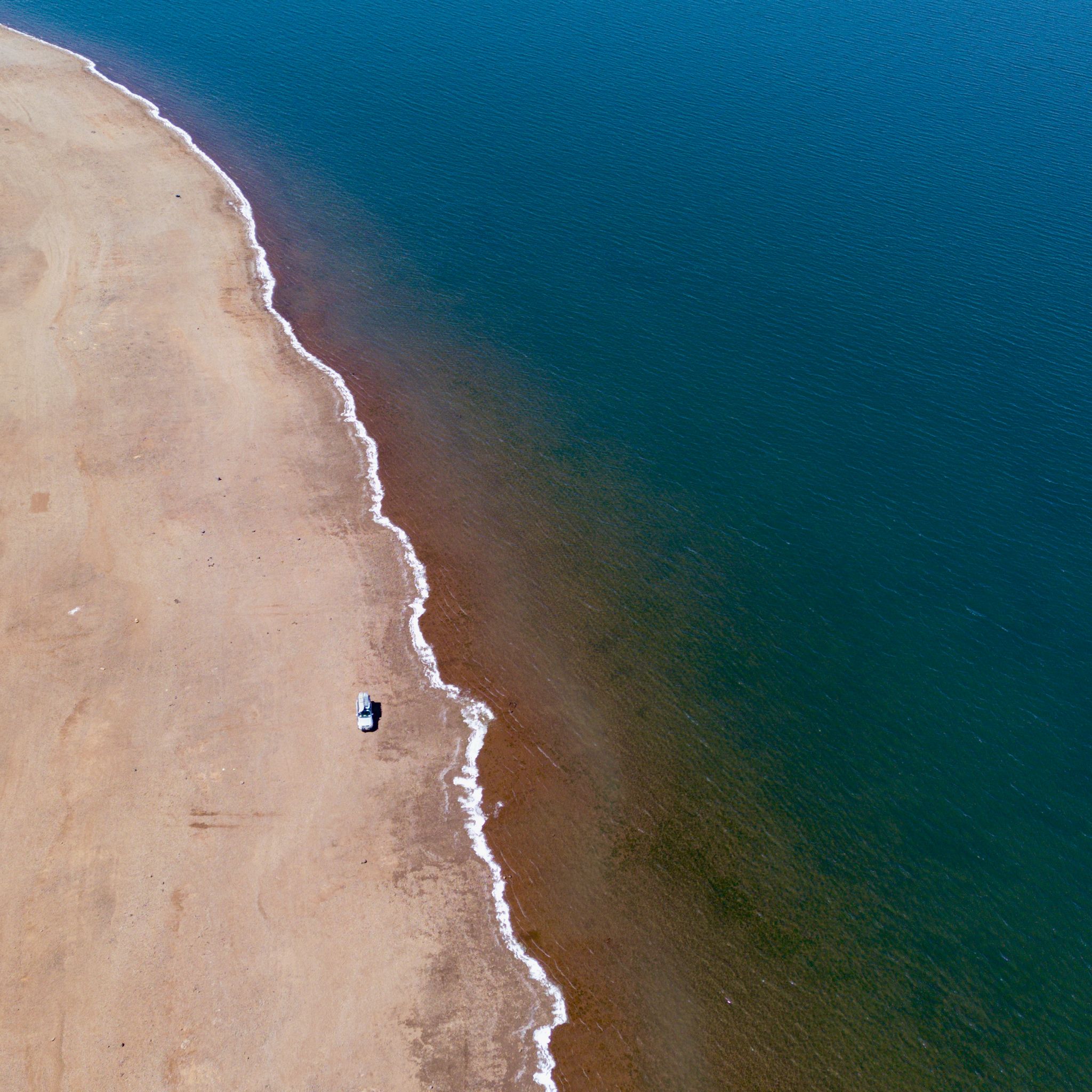 A picture taken from a drone of a car alongside the blue water of Yinga, the Great Lake.
